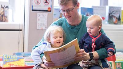 A photo of a dad reading to two children in the library