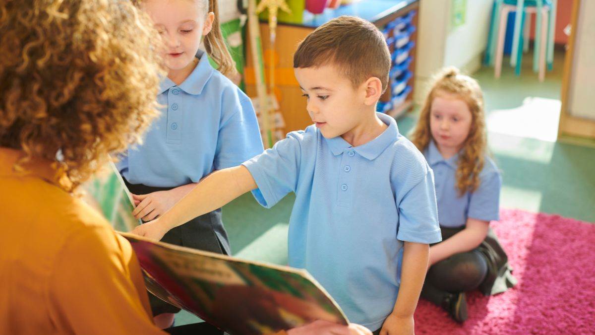 Children in school uniform looking at a book being held up by a teacher